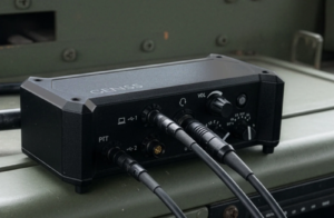 A rugged GENSS platform radio control unit mounted on the dashboard of a military vehicle, showing multiple connected cables, control dials and a durable enclosure designed for field operations.