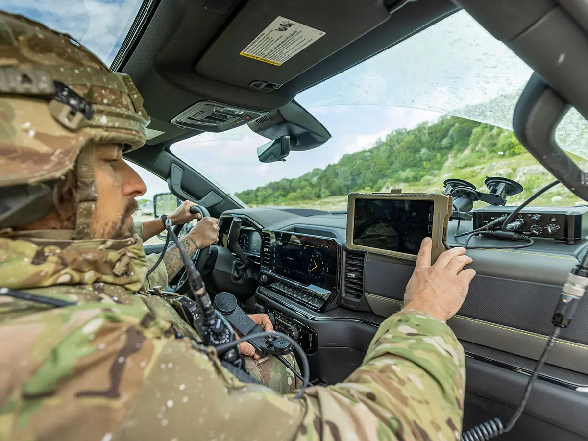 Military personnel operating tactical communications equipment inside a vehicle during a field exercise.